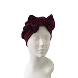 Burgundy velvet headband with bow on a mannequin head against a white background