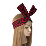 A red and black zebra-striped fabric headband with a large bow, displayed on a mannequin head with long blonde hair against a plain white background.