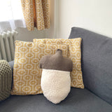 Decorative pillows and an acorn-shaped cushion on a sofa with curtains in the background.