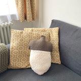 Decorative pillows and an acorn-shaped cushion on a sofa with curtains in the background.