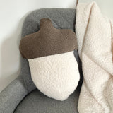 Textured pillow with brown top and white bottom on a gray chair with a beige blanket.