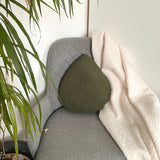 Gray armchair with a green cushion and white blanket, next to a plant.