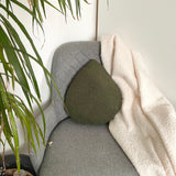 Gray armchair with a green cushion and white blanket, next to a plant.