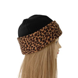 A black beanie hat with a leopard print fleece ear warmer band, displayed on a mannequin head with long blonde hair against a white background.