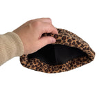 A hand wearing a beige knit sweater pulls open a leopard-print fabric pouch or pocket against a plain white background.