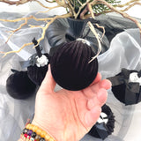 Black velvet hair bun holder with decorative bow held by a hand against a neutral background.