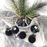 Black velvet ornaments with silver ribbons on a decorative arrangement with branches and greenery.
