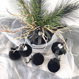 Black velvet ornaments with silver ribbons on a decorative arrangement with branches and greenery.