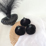 Black velvet pumpkins and a decorative vase on a textured surface