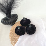 Black velvet pumpkins and a decorative vase on a textured surface