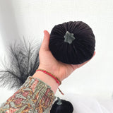 Hand holding a black velvet pumpkin with a gray center against a white background