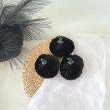 Black velvet pumpkins on a woven mat with decorative grasses on a light background