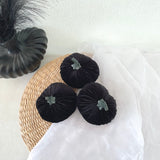 Black velvet pumpkins on a woven mat with a white background