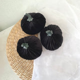 Three black velvet pumpkins on a woven mat with a white background