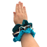 Hand wearing a blue scrunchie with a patterned design on a white background