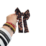 Hand holding a leopard print hair bow against a white background