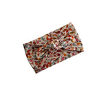 A fabric headband with a multi-colored autumn leaf pattern, featuring a central twist knot, shown on a plain white background.