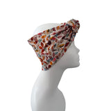 A multicolor leaf-patterned headwrap turban hat styled on a white mannequin head in profile against a solid white background.