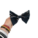 Navy blue bow tie with white patterns held by a hand on a white background
