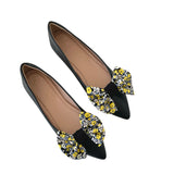 Black pointed-toe flats with floral bow details on a white background