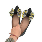 Black flats with floral bow details held by a hand on a white background
