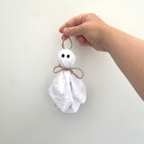 Hand holding a small white ghost decoration with a plain background