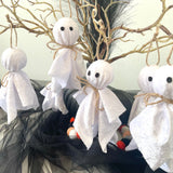 White ghost decorations with black eyes and mouths on a Halloween-themed background with branches and black tulle.
