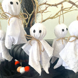 White ghost decorations with black eyes and orange candy corn on a Halloween-themed background.