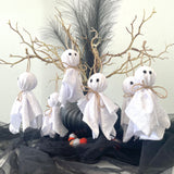 Halloween decorations with white ghost figures, candy, and branches on a black cloth.
