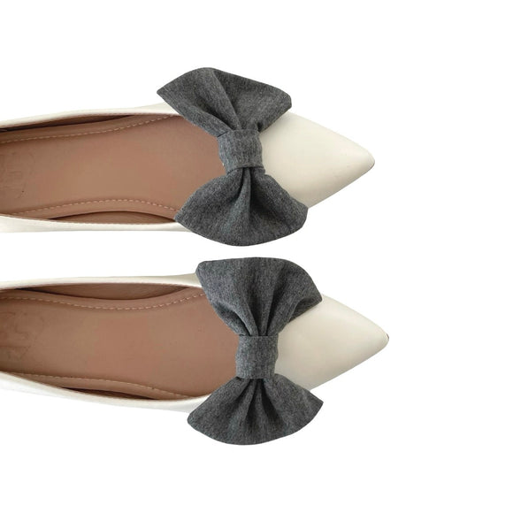 Gray bow-shaped shoe clips on beige shoes against a white background