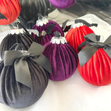 Decorative bags in black, purple, and rust with black bows on a white surface.