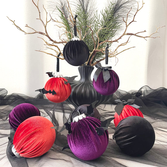 Halloween-themed ornaments in red, purple, and black on a decorative table with branches and tulle.