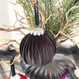 Black velvet ornament with decorative top hanging against a natural branch background