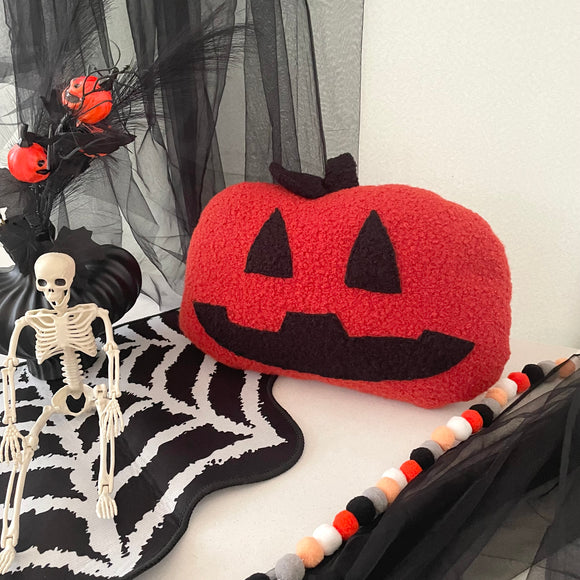 Halloween-themed decor with a red jack-o'-lantern pillow, skeleton, and spiderweb on a white background.