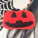 Red jack-o'-lantern-shaped pouch with black details on a Halloween-themed background.