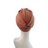 A ribbed knit turban-style beanie in a muted terracotta brown color, displayed on a white mannequin head against a plain white background.