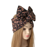 A leopard print hair bow headwrap displayed on a mannequin head with long blonde hair, set against a plain white background.