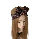 A black and brown leopard-print hair bow headband displayed on a mannequin head with long light brown hair against a plain white background.