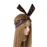 A leopard-print headband with a large bow on top, displayed on a mannequin head with long blonde hair against a plain white background.