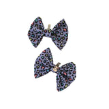 Two purple leopard print bows with gold clips on a white background