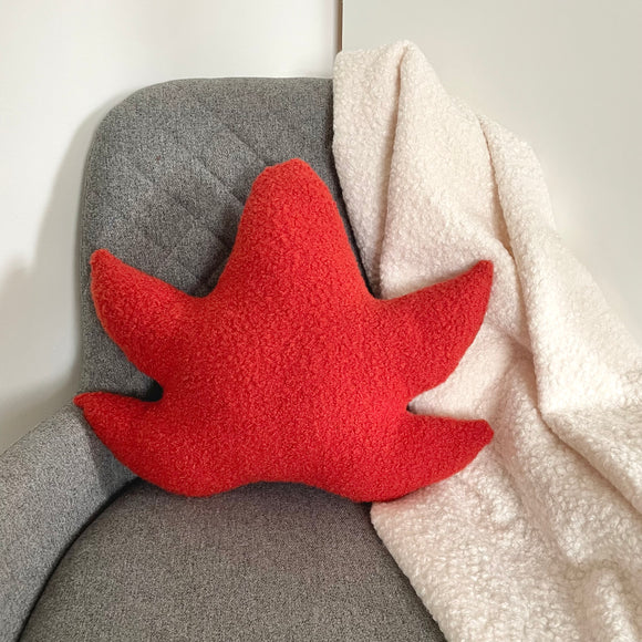 Red leaf-shaped pillow on a gray chair with a white blanket