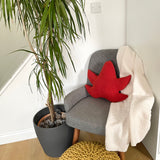 Gray armchair with a red leaf-shaped pillow next to a potted plant in a room.