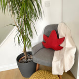 Gray armchair with a red leaf-shaped pillow next to a potted plant in a room.