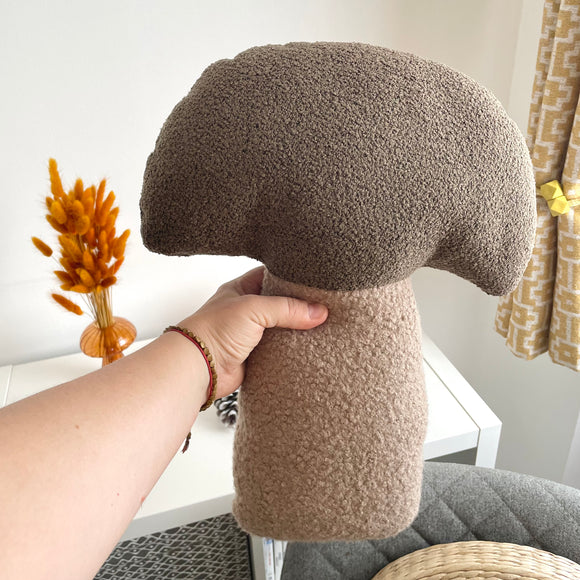 Hand holding a brown mushroom-shaped pillow against a neutral background