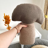Hand holding a brown mushroom-shaped pillow against a neutral background