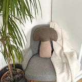 Gray armchair with a mushroom-shaped pillow and blanket, next to a potted plant.
