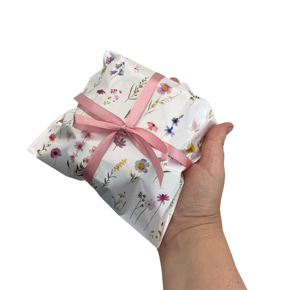 Hand holding a wrapped gift with floral pattern and pink ribbon on a white background