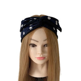 A navy blue fabric headband with white polka dots, styled on a mannequin head with long light brown hair against a plain white background.