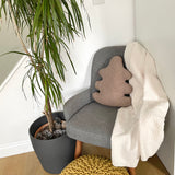 Gray armchair with a beige cushion and white blanket next to a potted plant in a room.