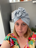 Woman wearing a colorful top and gray headscarf indoors.